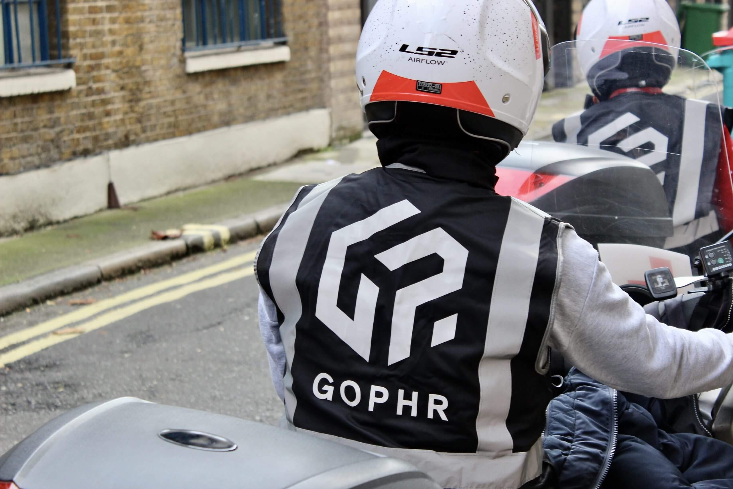 Two Gophr motorbike couriers in branded gilets handing over a delivery
